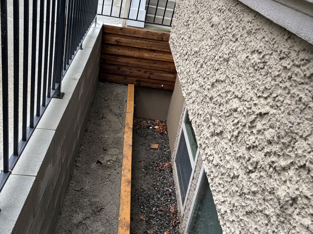 Window-well retaining wall with cedar trim, gravel bed and black railing